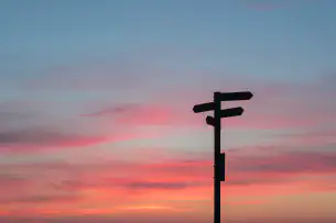 A silhouette of a directional sign at sunset.