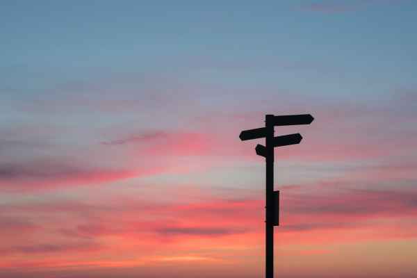 A silhouette of a directional sign at sunset.