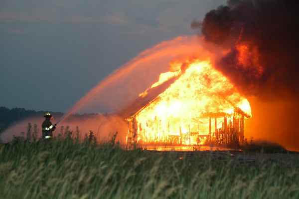 A fireman using a firehose to put out a flaming old building.