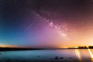 A shooting star and the milkyway seen at sunset above a lake.