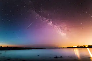 A shooting star and the milkyway seen at sunset above a lake.